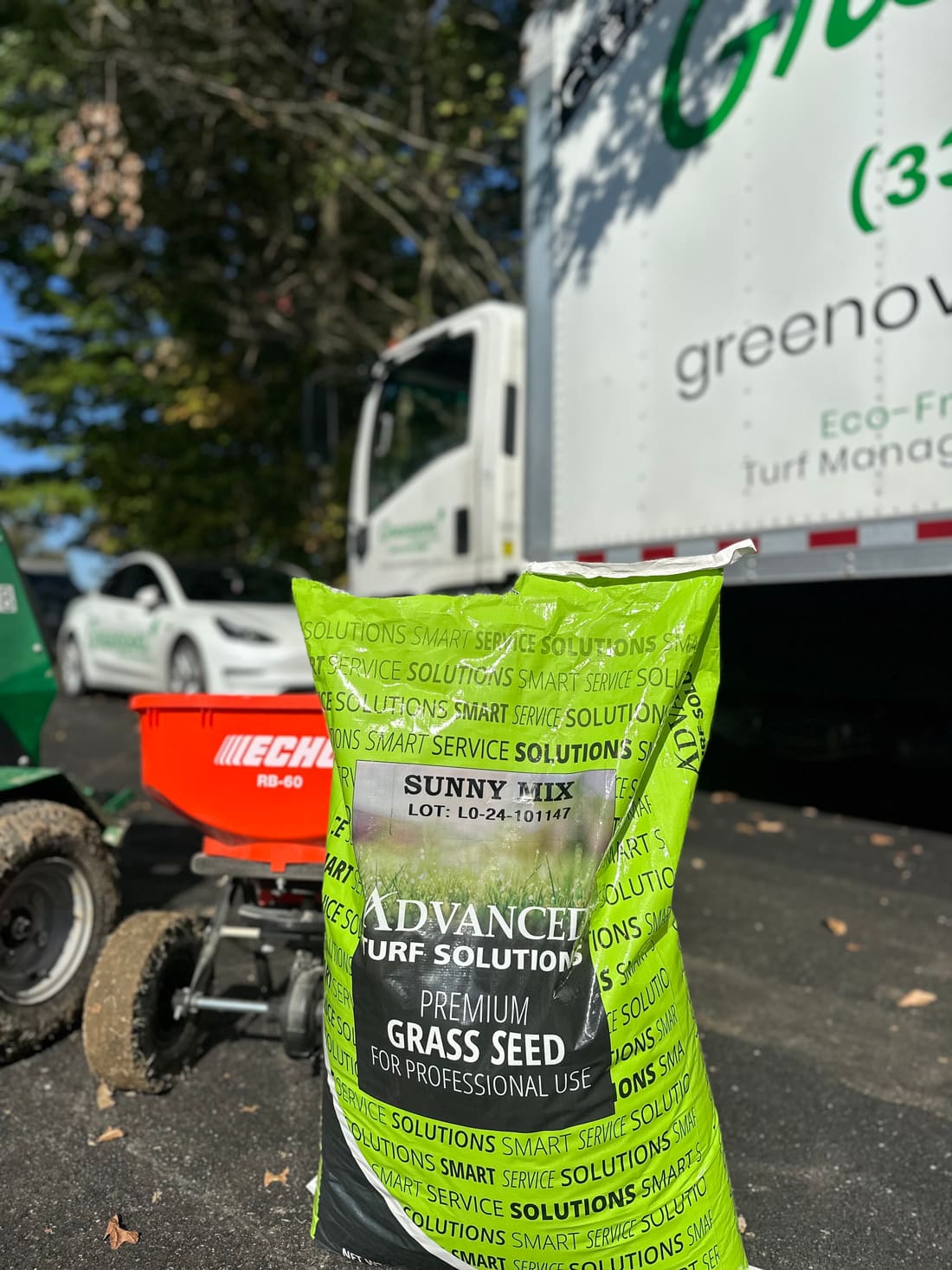 A bag of premium professional-grade grass seed beside a Greenova Fertilization service truck